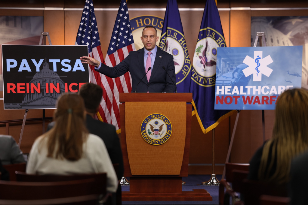 Leader Jeffries Speaking at Weekly Press Conference in between posters that read "Pay TSA Rein In Ice" and "Healthcare Not Warfare"