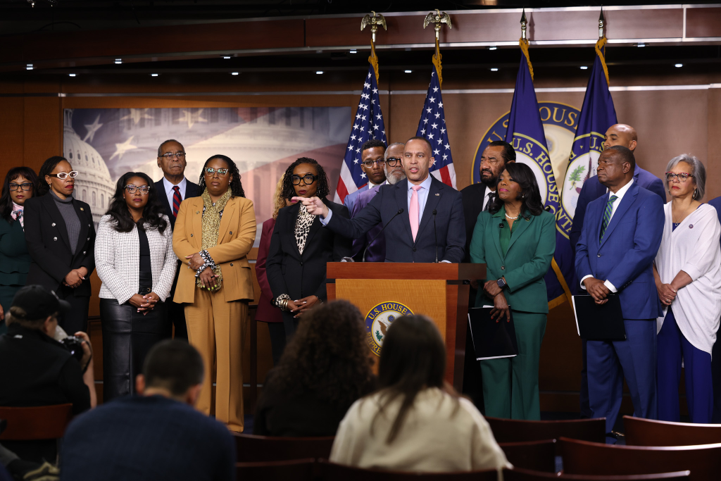 Leader Jeffries speaking at press conference from behind a podium with members of the Congressional Black Caucus