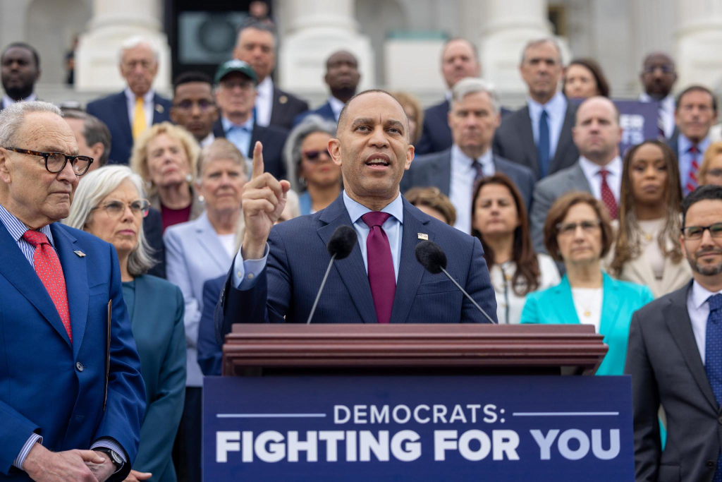 Leader Jeffries (center) speaking from a podium with a sign reading "Democrats Fighting for You"